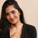 Rukmini Vasanth wearing a black top and relaxed light-wash jeans in a warm studio portrait
