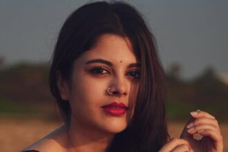 Sanjana Krishnamoorthy wearing a deep maroon handloom saree by the sea