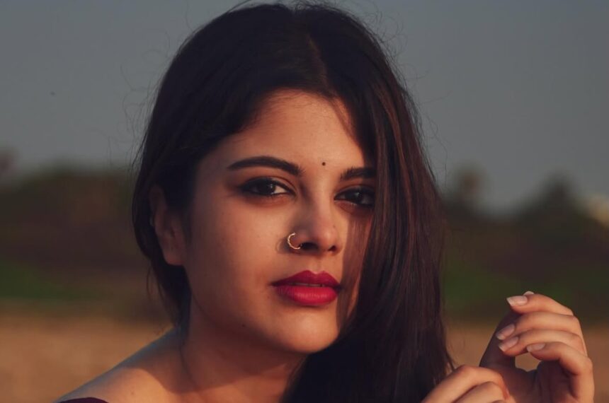 Sanjana Krishnamoorthy wearing a deep maroon handloom saree by the sea