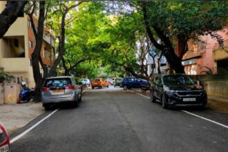 Evening view of Bengaluru's Indiranagar 100 Feet Road with tree-lined streets, cafés, restaurants and pedestrians.
