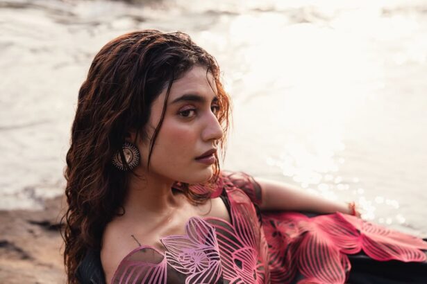 Priya Prakash Varrier posing in a sculptural pink couture outfit beside a flowing river during a fashion photoshoot.