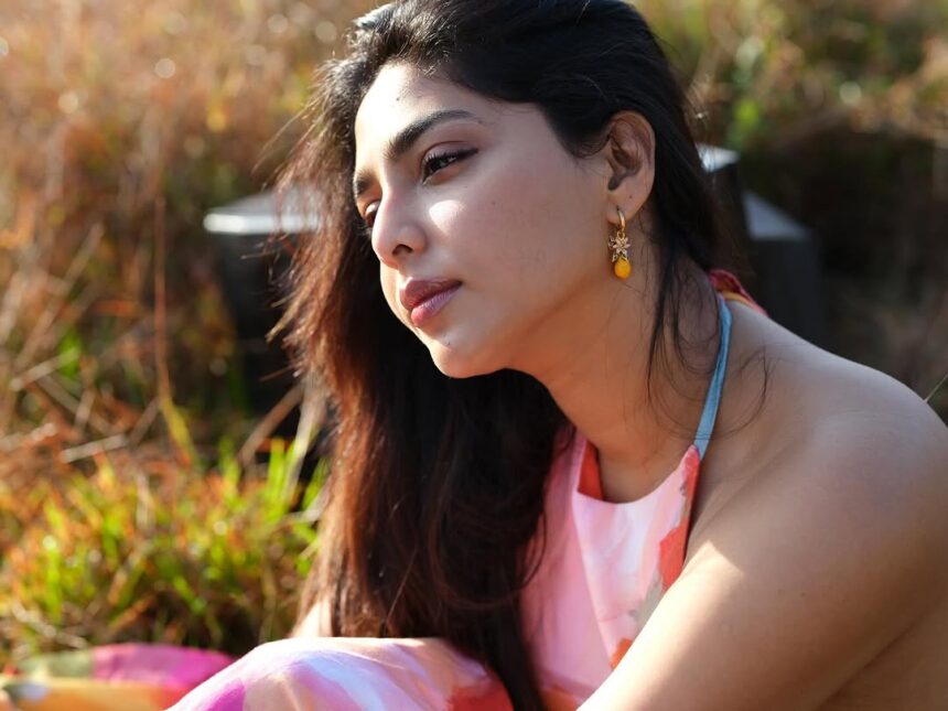 Aishwarya Lekshmi wearing a vibrant floral outfit during a golden-hour outdoor photoshoot in a lush green field.