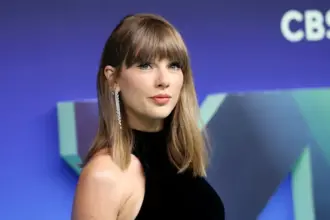 Taylor Swift with curly blonde hair wearing a maroon sweater