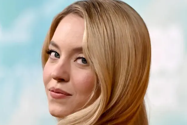 Sydney Sweeney wears long blonde waves with a leather bomber jacket and jeans.