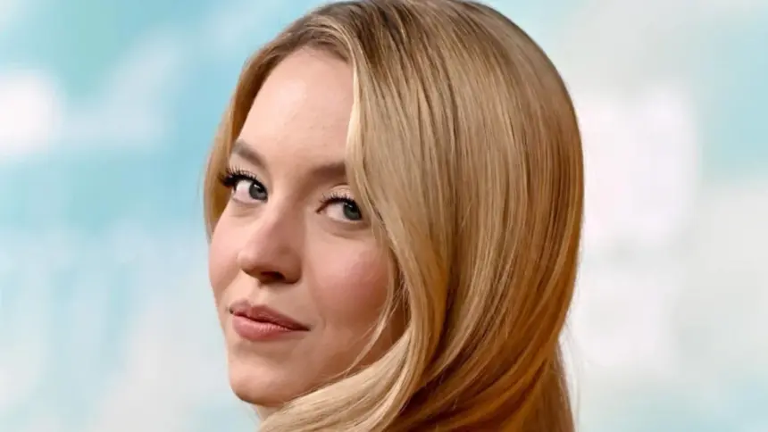 Sydney Sweeney wears long blonde waves with a leather bomber jacket and jeans.